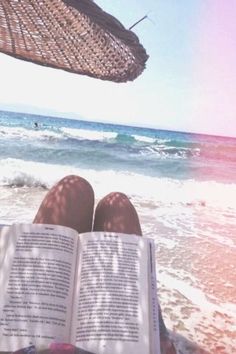 someone is reading a book on the beach with their feet in the sand and water