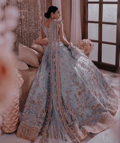 a woman in a blue and gold wedding dress sitting on a bed next to a window