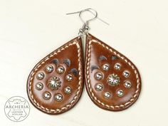 Handcrafted leather earrings with unique and eye catching details. Each earring features hand stitching, slick edges and centered hand stamping, accented with beautiful small rivets. Surgical stainless steel earring hooks completes the look! The vegetable tanned leather is antiqued tan and sealed. Available in many colors, just ask!  *Width 3,7 cm (1,45"), height 5,8 cm (2,28") without hook, depth 8,4 mm (0,33") *total leather thickness 5-6 mm (0,19-0,23") *Cowhide, vegetable-tanned *Weight: 7 g (0,25 oz.) *Earring hooks:  Surgical stainless steel *Including organzabag and silicone rubber ear nuts *Shipping with tracking number With use and exposure to the elements, the leather changes colour and develops its own unique patina, which is distinctive of leather. In my prices is in accordance Slick Edges, Earring Hooks, Handcrafted Leather, Stainless Steel Earrings, Leather Earrings, Vegetable Tanned Leather, Rivets, Hand Stitching, Favorite Jewelry