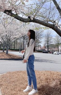 a woman standing under a tree in the middle of a park with flowers on it