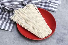 a red plate topped with spaghetti next to a black and white checkered napkin on top of a gray surface