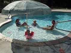 three women and two children in a pool with an umbrella over the kiddie area