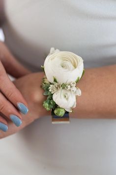 a woman's arm with a white flower and greenery on it, while wearing a ring