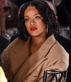 a close up of a person sitting at a table wearing a brown coat and red lipstick