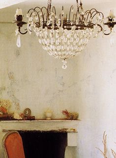 a chandelier hanging from the ceiling in a room with a fireplace and chair