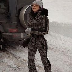 a woman standing in the snow next to a vehicle with her hand on her hip