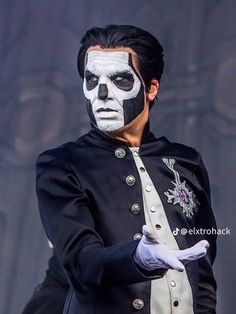 a man with white face paint on his face and black hair, wearing a costume