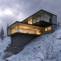 a house on top of a snowy hill in the evening with its windows lit up