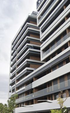 an apartment building with many balconies and plants in the foreground, on a cloudy day