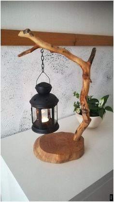 a wooden table topped with a lamp next to a tree branch and potted plant