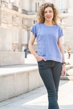 a woman with curly hair standing in front of a building and smiling at the camera