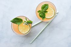 two glasses filled with lemonade and basil on top of a white countertop next to green straws