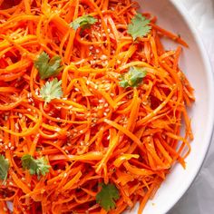 a glass bowl filled with shredded carrots and herbs next to a wooden spatula