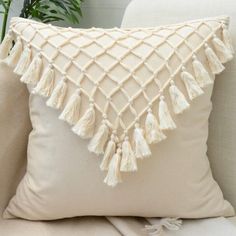 a white pillow with tassels on it sitting on a couch next to a potted plant