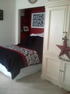 a bedroom with red and black bedding, white cabinets and a star hanging on the wall