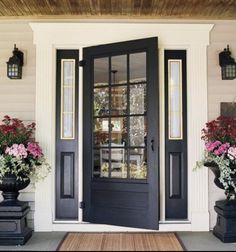 the front door is painted black and has flowers in large urns on either side