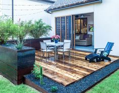 a patio with wooden decking and blue chairs next to a white house in the background