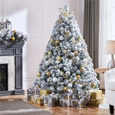 a white christmas tree with gold and silver ornaments on it in front of a fireplace