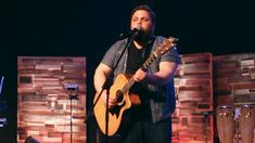 a man standing in front of a microphone while holding a guitar