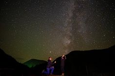 two people standing on top of a hill under the stars