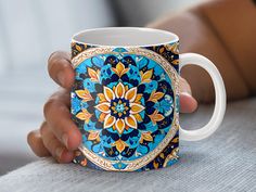 a person holding a coffee mug with colorful designs on it