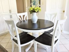 a black and white dining table with four chairs next to a vase filled with flowers