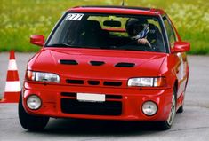 a red car driving down the road with a helmet on it's headlight