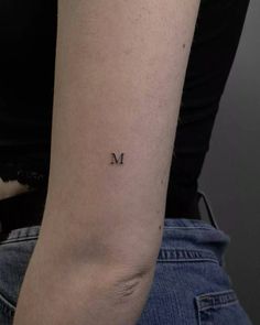 a woman's arm with the letter m tattooed on her left arm, in black ink