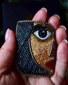 a hand holding a small beaded case with an eye on the front and side