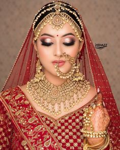 a woman in a red bridal outfit with gold jewelry on her face and hands