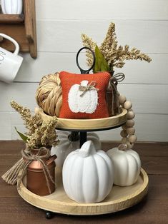 a three tiered tray with pumpkins and other decorative items on it, sitting on a wooden table