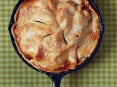 an apple pie in a cast iron skillet on a green checkered tablecloth