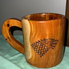 a wooden mug with a game of throne logo on it sitting on a green cloth