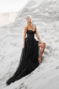 a woman in a black dress is sitting on the sand and posing for a photo