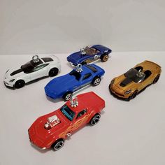 four toy cars are lined up on a white surface, one is red and the other two are blue