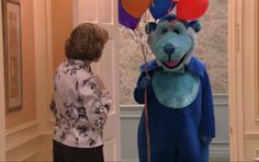 a woman standing next to a blue bear mascot holding balloons