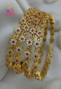 Material: High-quality gold plating on durable alloy Stones: Ruby and clear stones arranged in a floral pattern Design: Intricate floral design with a modern twist Set: 4 bangles  Size: Available in 2.4, 2.6, 2.8 and 2.10 sizes for a perfect fit Finish: Lustrous gold plating for a radiant look Key Features: Premium Quality: Made with superior materials to ensure long-lasting shine and durability. Elegant Design: The combination of gold and multi-color stones creates a timeless and versatile piec Statement Bangles, Ad Bangles, Designer Bangles, Ruby Bangles, Gold Jewellry, American Diamond Necklaces, Fleur Design, Bangles Set, Gold Plated Bangles