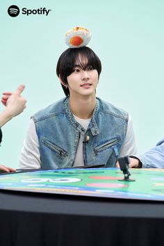 the young man is sitting at a table with an object on top of his head