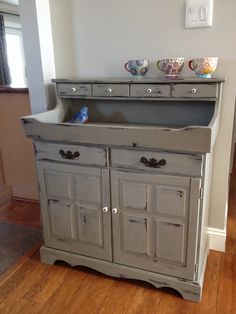 an old dresser is painted gray and has two cups on it's top shelf