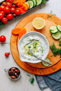 a bowl of dip with cucumbers, carrots and tomatoes on the side