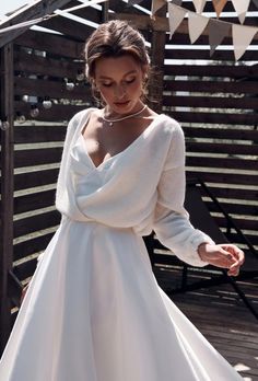 a woman in a white dress is standing on a wooden deck and looking down at her hand