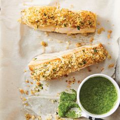 two fish fillets sitting on top of a piece of paper next to a cup of green sauce