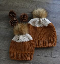 two knitted hats with brown and white pom - poms sitting on top of a wooden floor