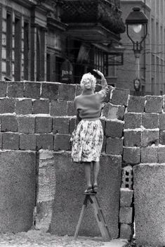 a woman standing on top of a ladder next to a pile of bricks in front of a building