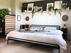 a bed with white sheets and pillows in a bedroom next to a dresser filled with potted plants