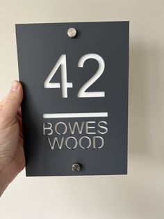 a person holding up a sign that says 422 bowes wood in silver letters