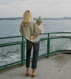 a woman holding a baby while standing on top of a pier