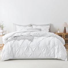 a bed with white comforter and pillows in a room next to a basket on the floor