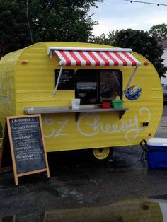 a yellow food truck with a red and white awning next to a chalkboard sign