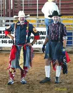 two men in costume standing next to each other on a dirt ground with a fence behind them